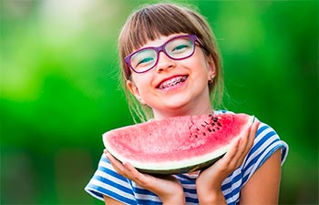 Happy girl with orthodontic braces holding a piece of watermelon.