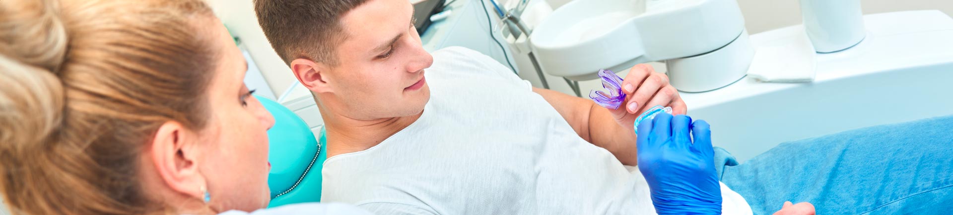 Female dentist showing a mouth guard to a sporty young man in a dental chair.