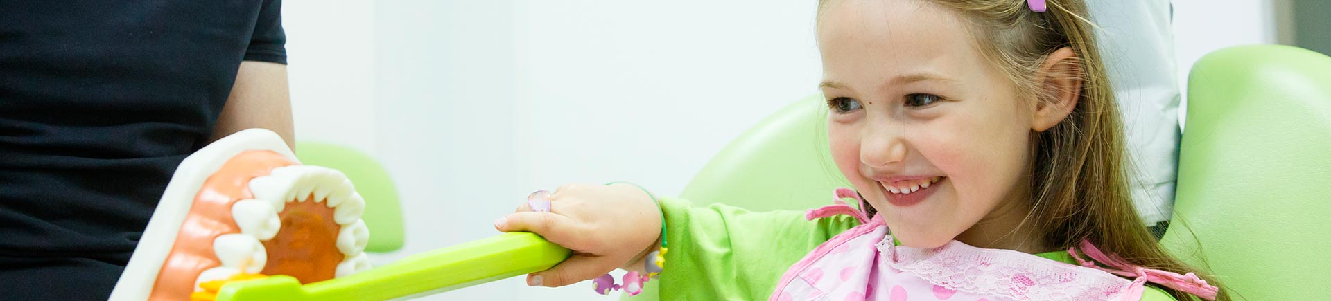 Smiling little girl in dentists chair being educated about proper tooth-brushing by her paediatric dentist