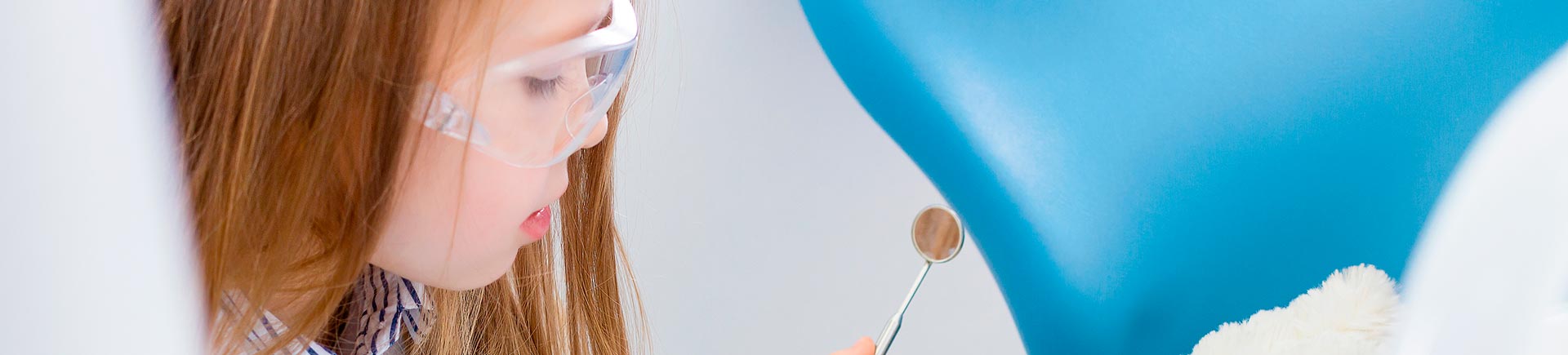 Little girl pretending to be a dentist while playing with her teddy-bear.