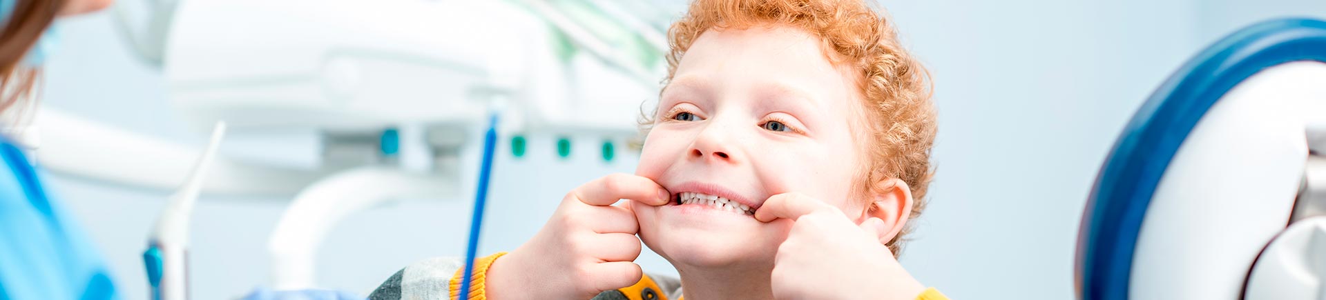 Little red-haired boy in a dentist treatment room showing his teeth.