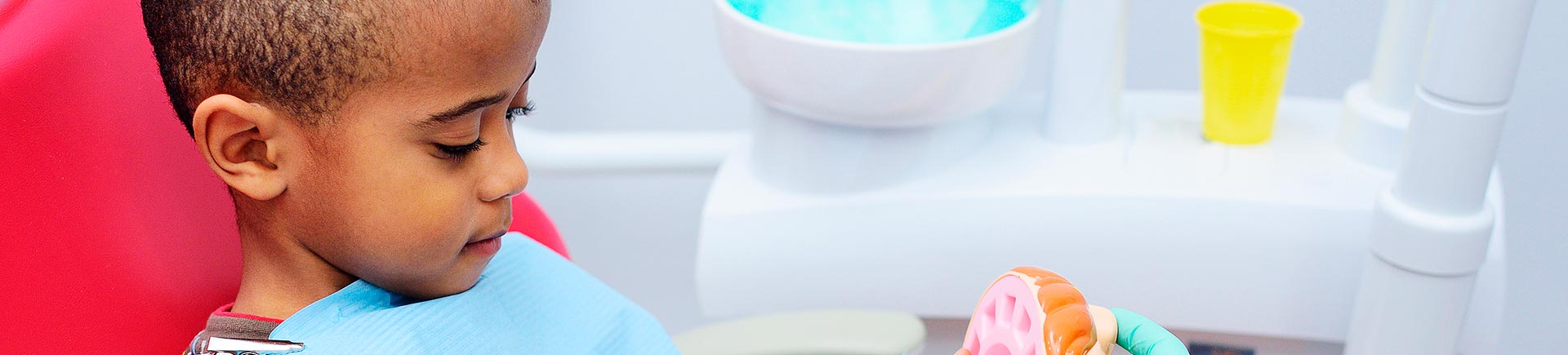 Little Afro-American boy in a dental chair being educated how to brush teeth.