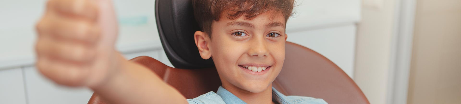 Cheerful young boy smiling in a dental chair showing his thumb up.