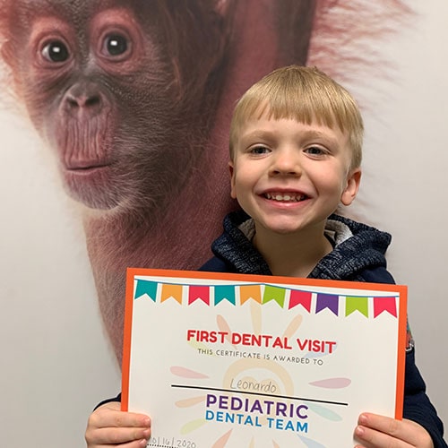 a young boy holding a diploma for his first dental visit