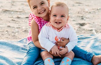 Two happy babies sitting on a blanket on the beach.