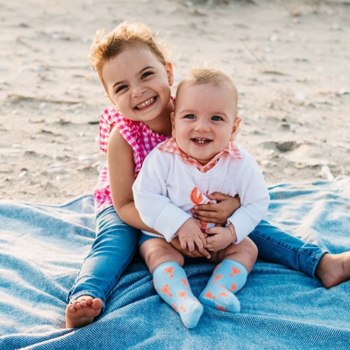 two kids sitting on a blanket, the girl is embracing a boy