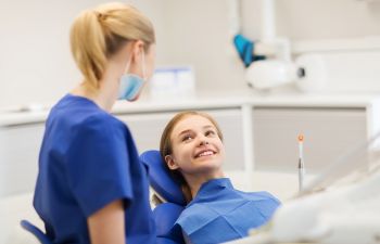 A dentist talking to a girl patient in a dental chair.