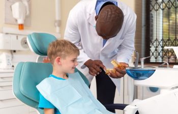 A boy in a dental chair and a dentist holding mouthguard aligner.